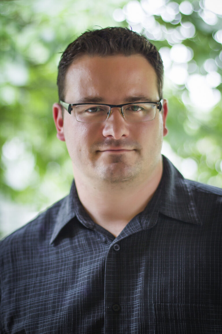 Portrait professionnel de Sylvain Beauchesne, propriétaire de Yéti Propre, debout devant un arrière-plan flou de verdure.